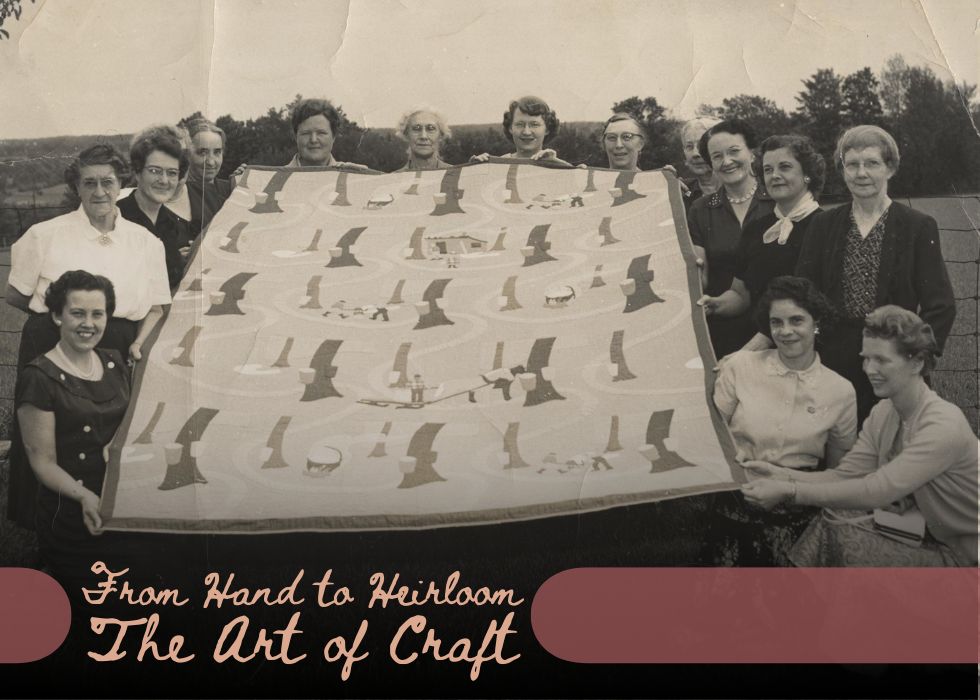 Women holding a large handmade quilt outdoors, historical photograph highlighting traditional craft and textile heritage.